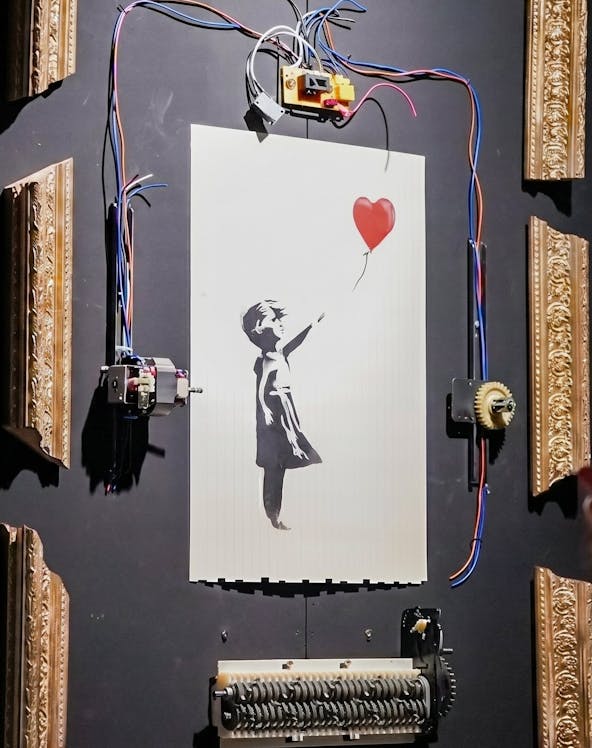 Banksy's "Girl with Red Balloon" artwork with mechanical frame at Banksy Limitless exhibit.