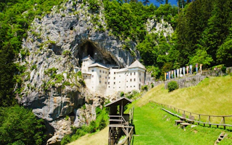 Castle Predjama nestled in a cliffside, surrounded by lush greenery in Slovenia.