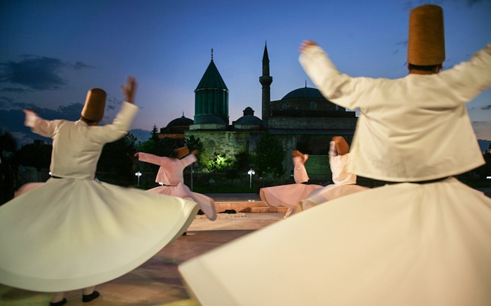 Whirling dervishes performing Mevlevi Sema in front of Istanbul mosque at dusk.