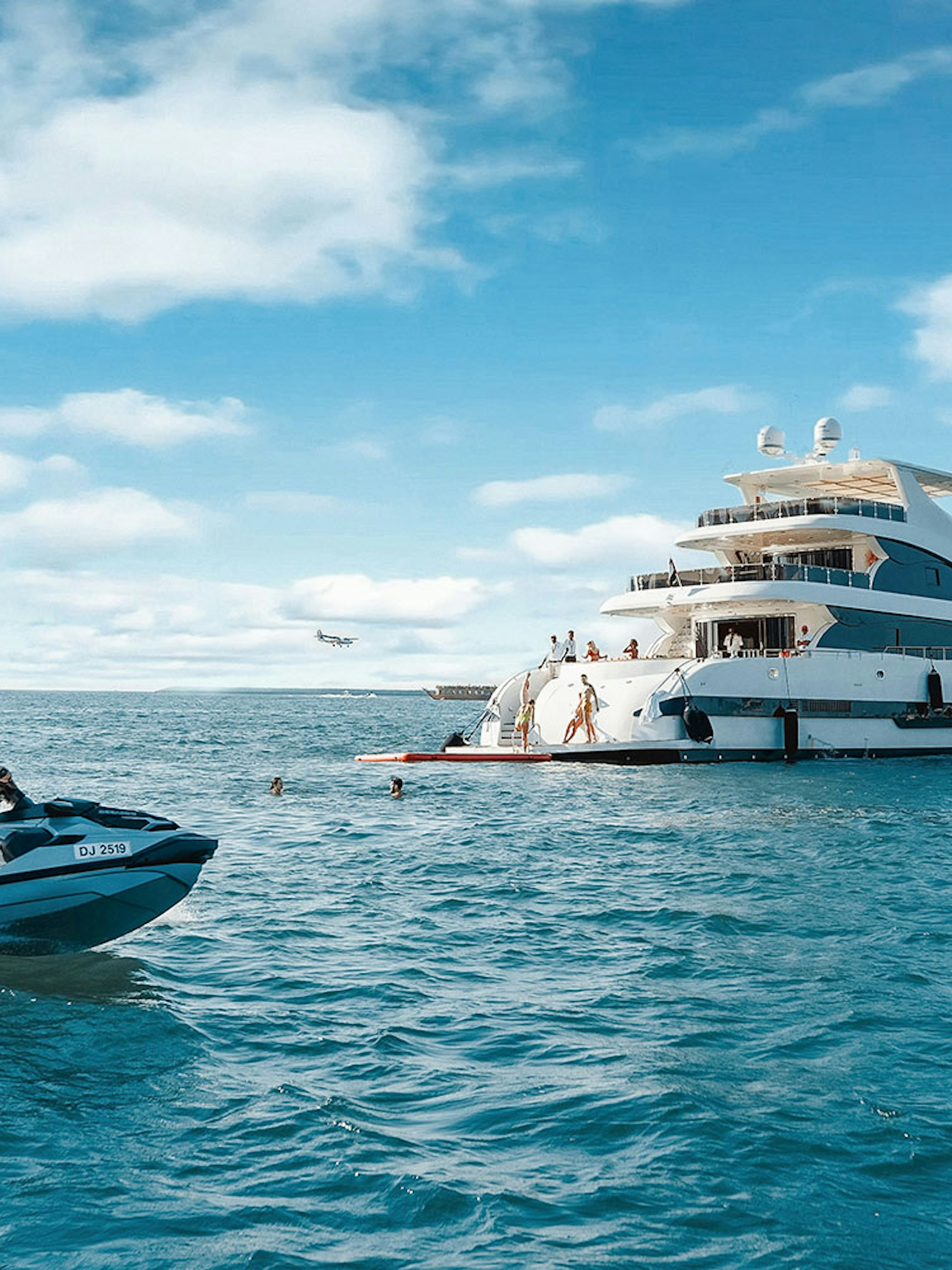 Jet ski near a TriDeck superyacht cruise with people enjoying the water.