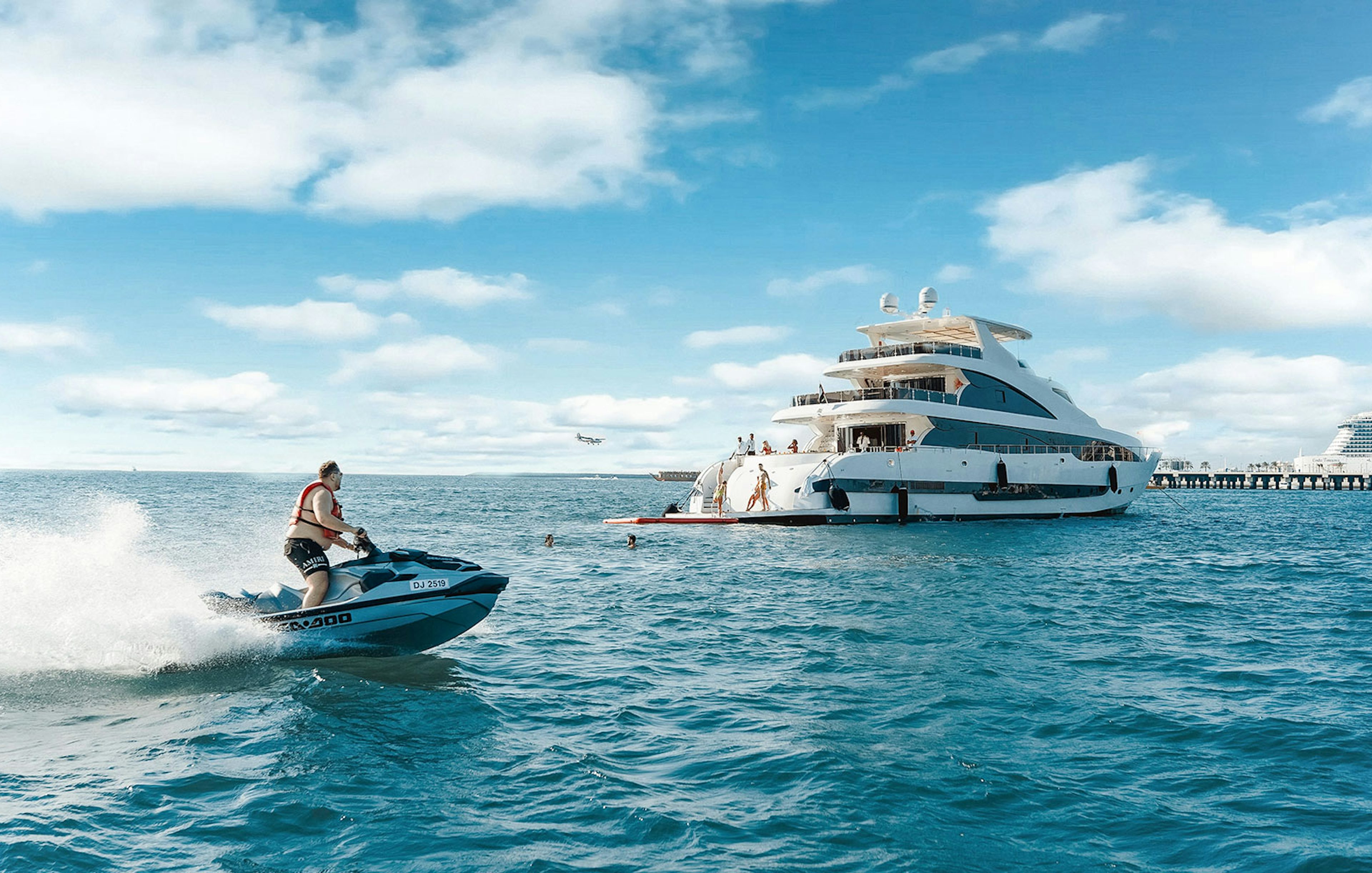 Jet ski near a TriDeck superyacht cruise with people enjoying the water.