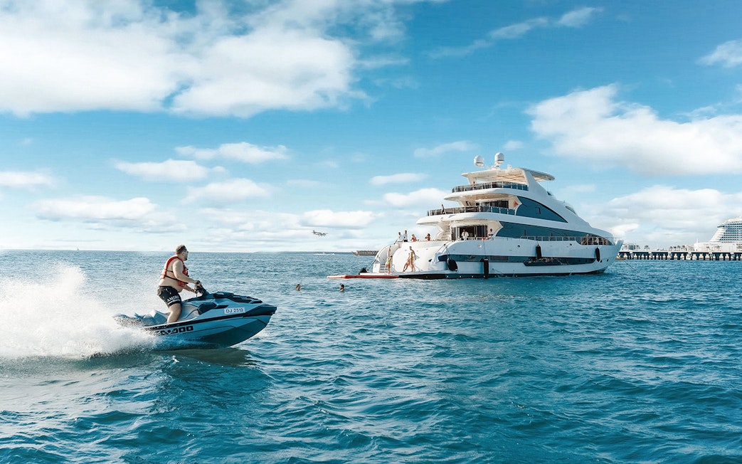 Jet ski near a TriDeck superyacht cruise with people enjoying the water.