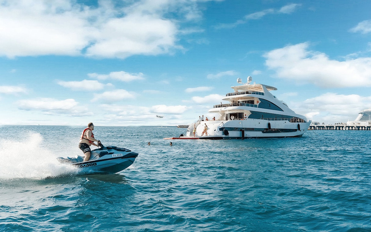 Jet ski near a TriDeck superyacht cruise with people enjoying the water.