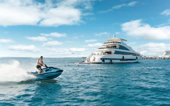 Jet ski near a TriDeck superyacht cruise with people enjoying the water.