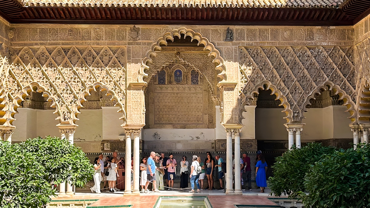 Alcazar of Seville courtyard with intricate arches and lush gardens during guided tour.
