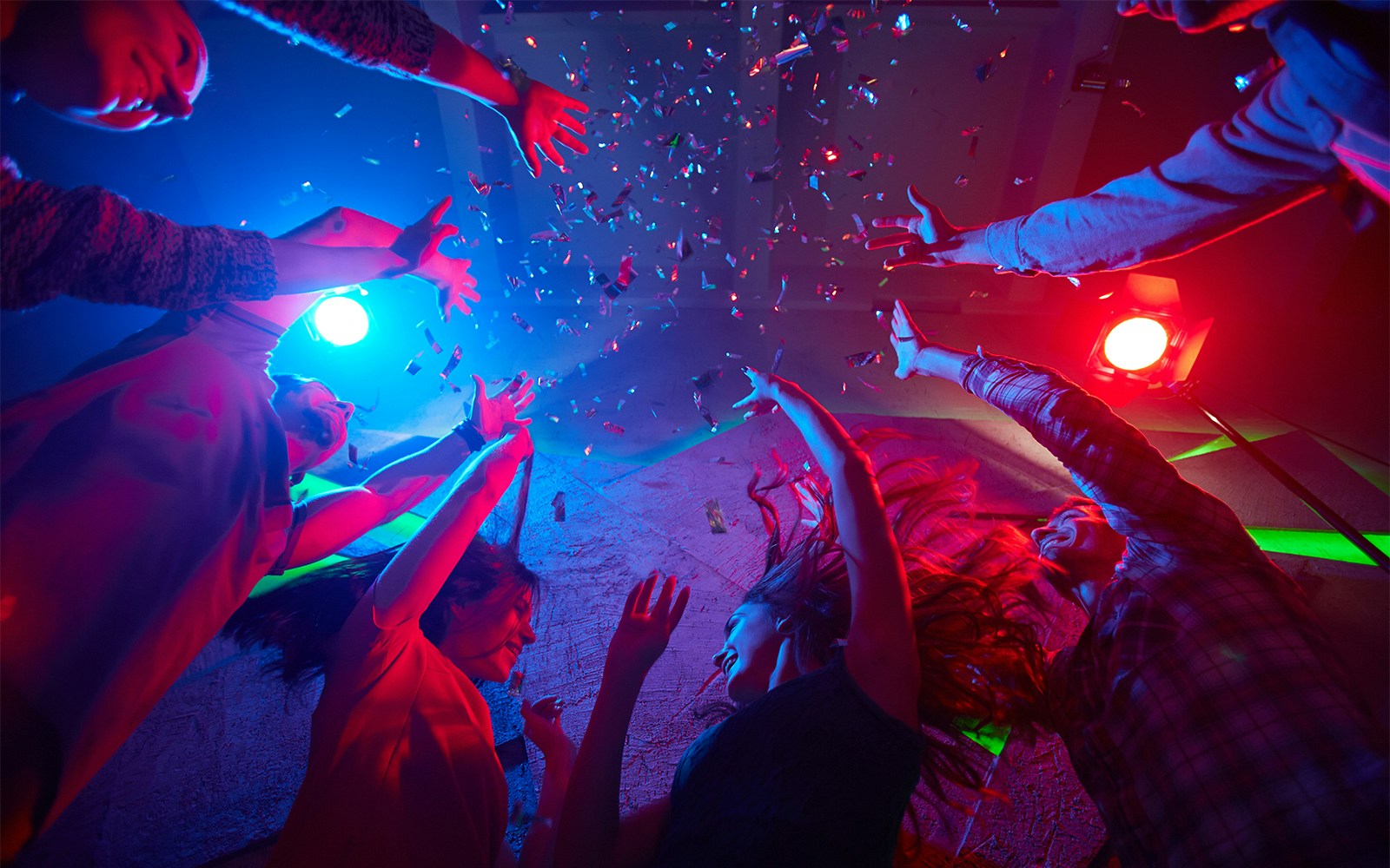People dancing under colorful lights at a techno party, confetti falling around them.