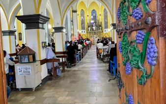 Interior of a church in Dar es Salaam with people attending a service, seen from an ornate wooden door.