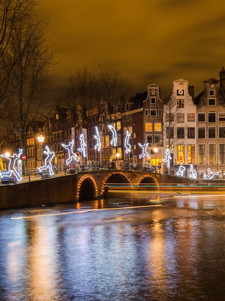 Amsterdam Light Festival illuminated figures on canal bridge at night.
