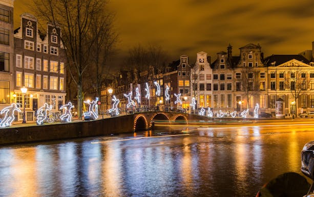 Amsterdam Light Festival illuminated figures on canal bridge at night.