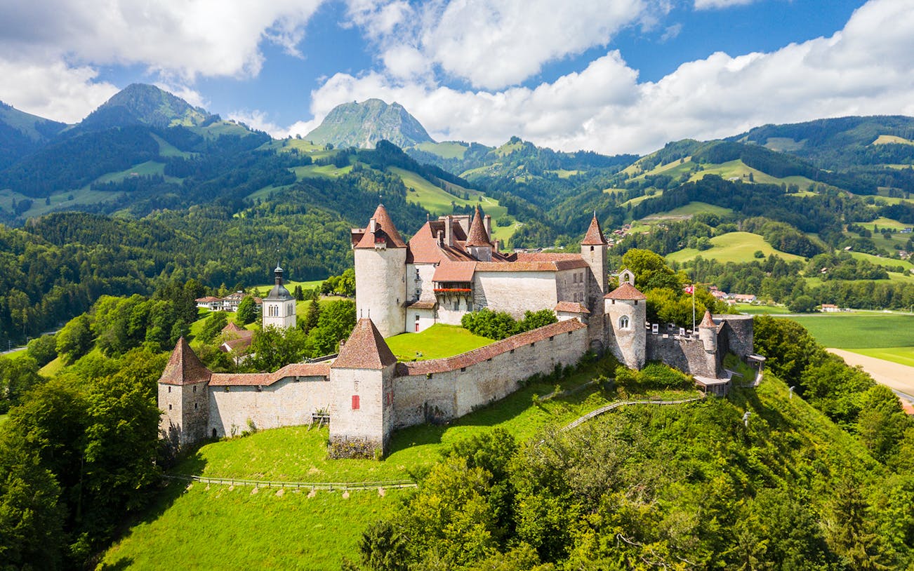 Gruyères Castle surrounded by lush green hills and mountains in Switzerland.