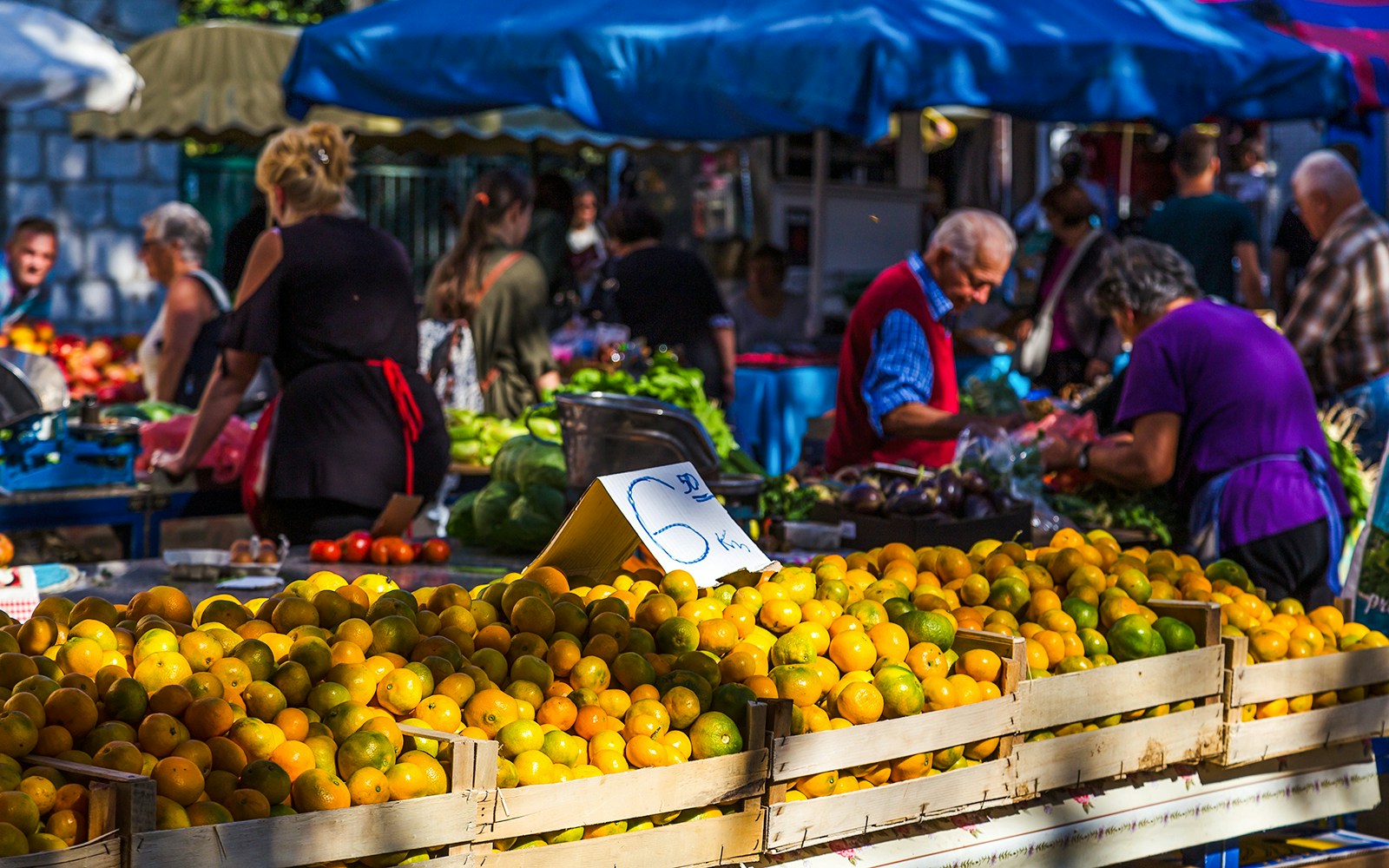 Crates of clementines at a bustling outdoor market with shoppers in the background.