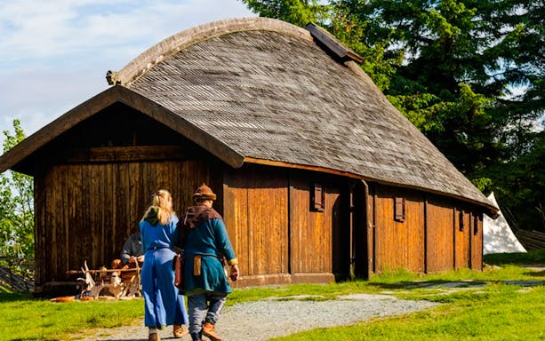 Viking reenactors walking towards a traditional longhouse in Avaldsnes.