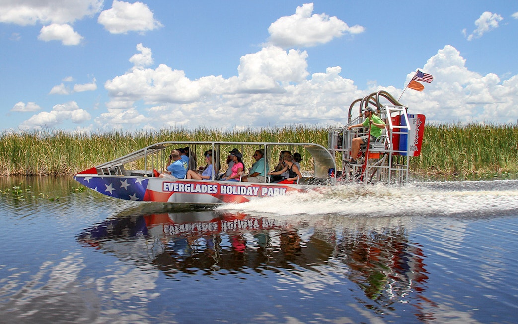 Everglades airboat tour with passengers gliding through wetlands under a clear sky.