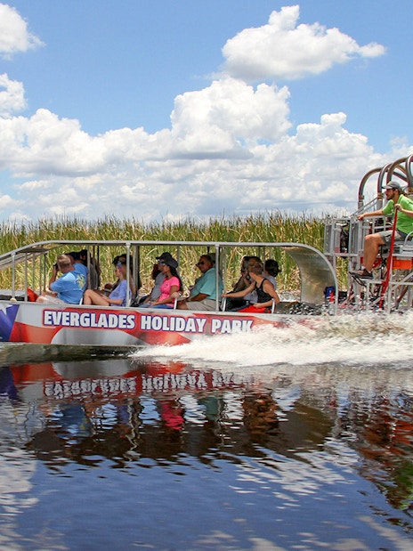Everglades airboat tour with passengers gliding through wetlands under a clear sky.