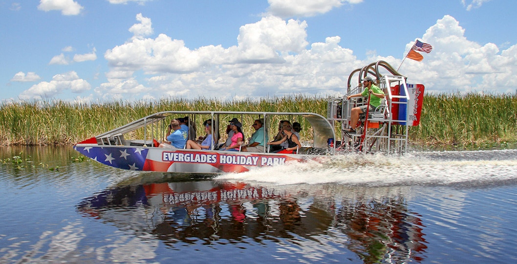 Everglades airboat tour with passengers gliding through wetlands under a clear sky.