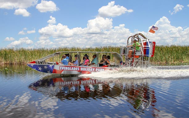 Everglades airboat tour with passengers gliding through wetlands under a clear sky.