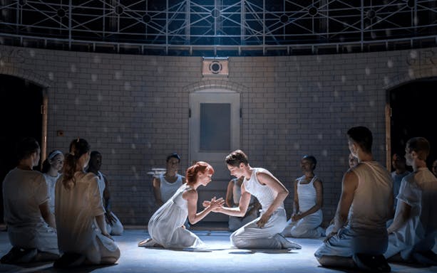 Dancers perform a scene from Matthew Bourne's Romeo and Juliet, surrounded by a seated ensemble.