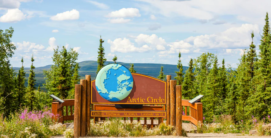 Arctic Circle sign on Dalton Highway, Alaska, surrounded by forest and mountains.