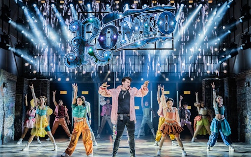 Performers on stage during a scene from the musical "& Juliet" with a "Romeo" sign above.
