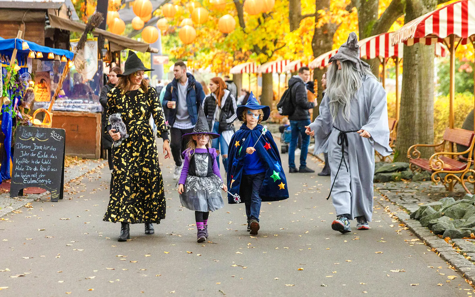 Families in Halloween costumes walking through Heide Park decorated with autumn leaves and lanterns.