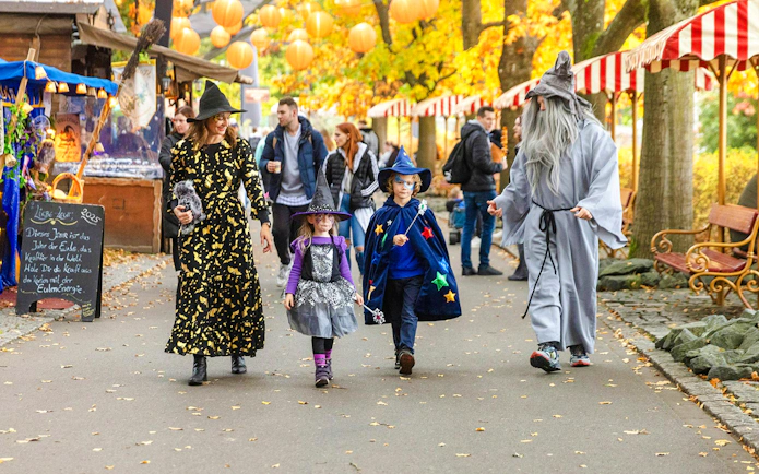 Families in Halloween costumes walking through Heide Park decorated with autumn leaves and lanterns.