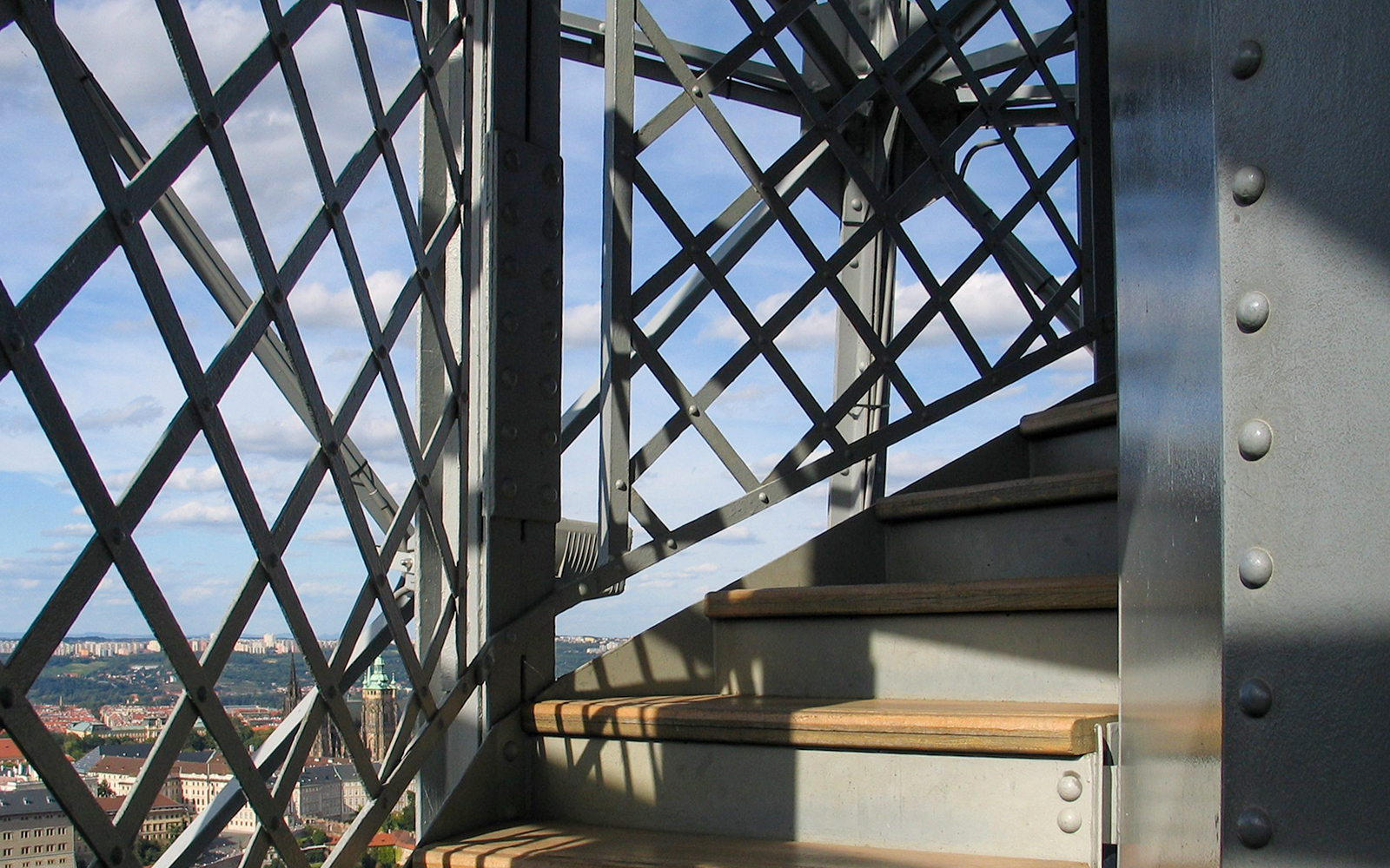 Stairs inside Petrin Tower with a view of Prague through metal lattice.