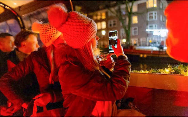 Guests enjoying a canal cruise in the Red-Light District, Amsterdam, with drinks and city views.