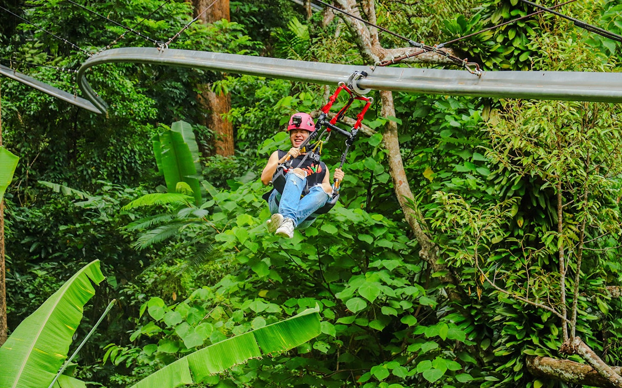 Girl enjoying roller zipline through lush forest.