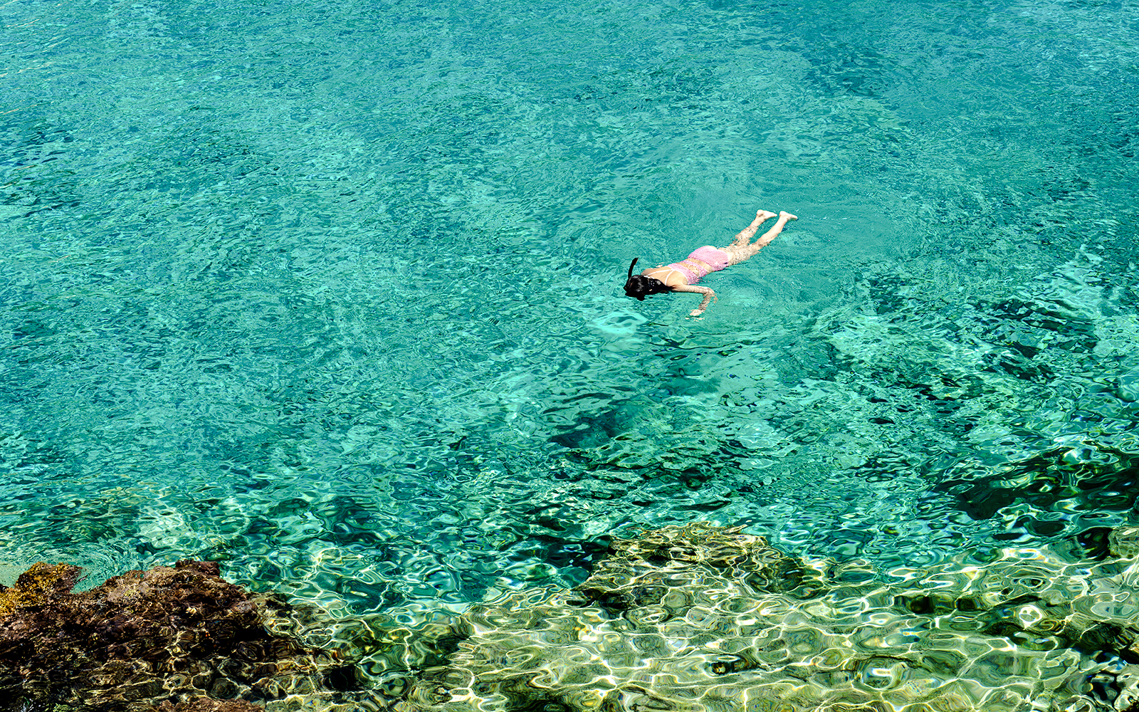 Woman snorkeling in clear turquoise water near a rocky reef.