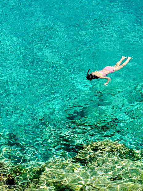Woman snorkeling in clear turquoise water near a rocky reef.