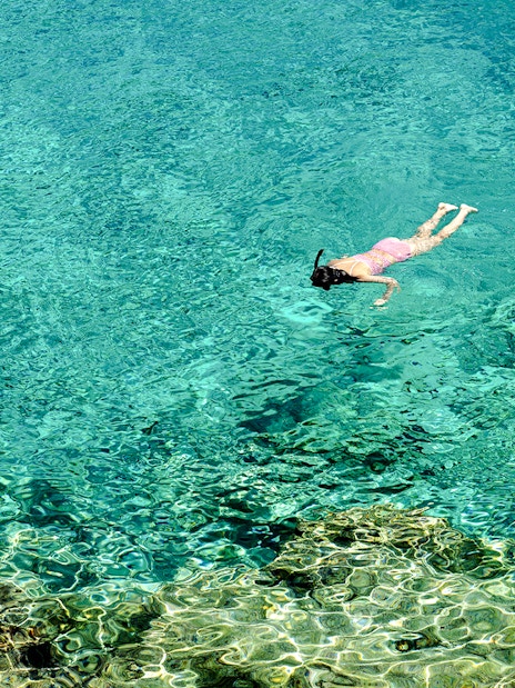 Woman snorkeling in clear turquoise water near a rocky reef.