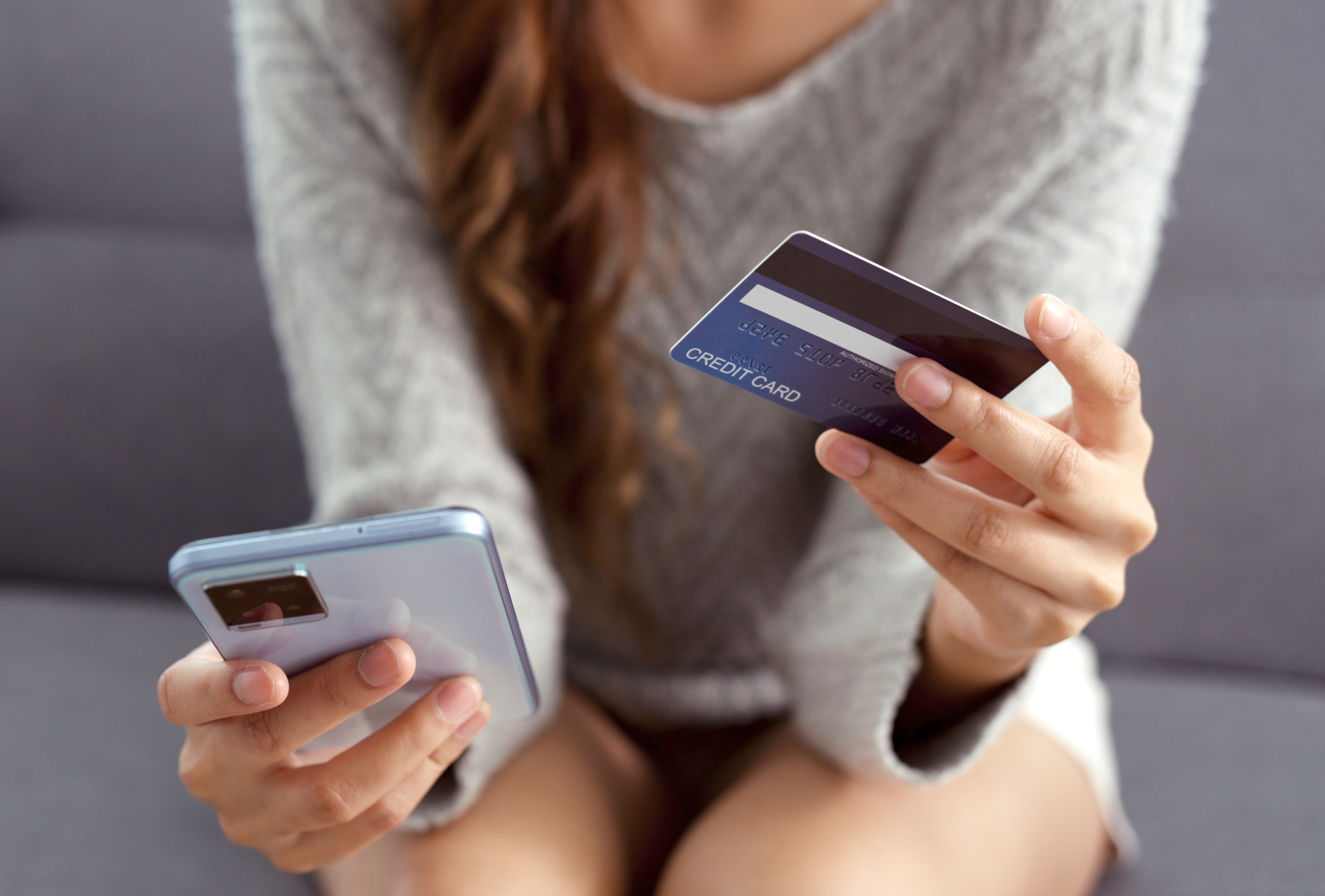 Eine auf einer Bank sitzende Frau hält eine Kreditkarte und ein Smartphone in der Hand