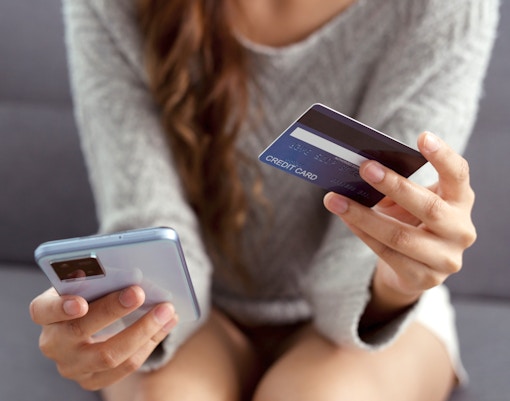 Eine auf einer Bank sitzende Frau hält eine Kreditkarte und ein Smartphone in der Hand