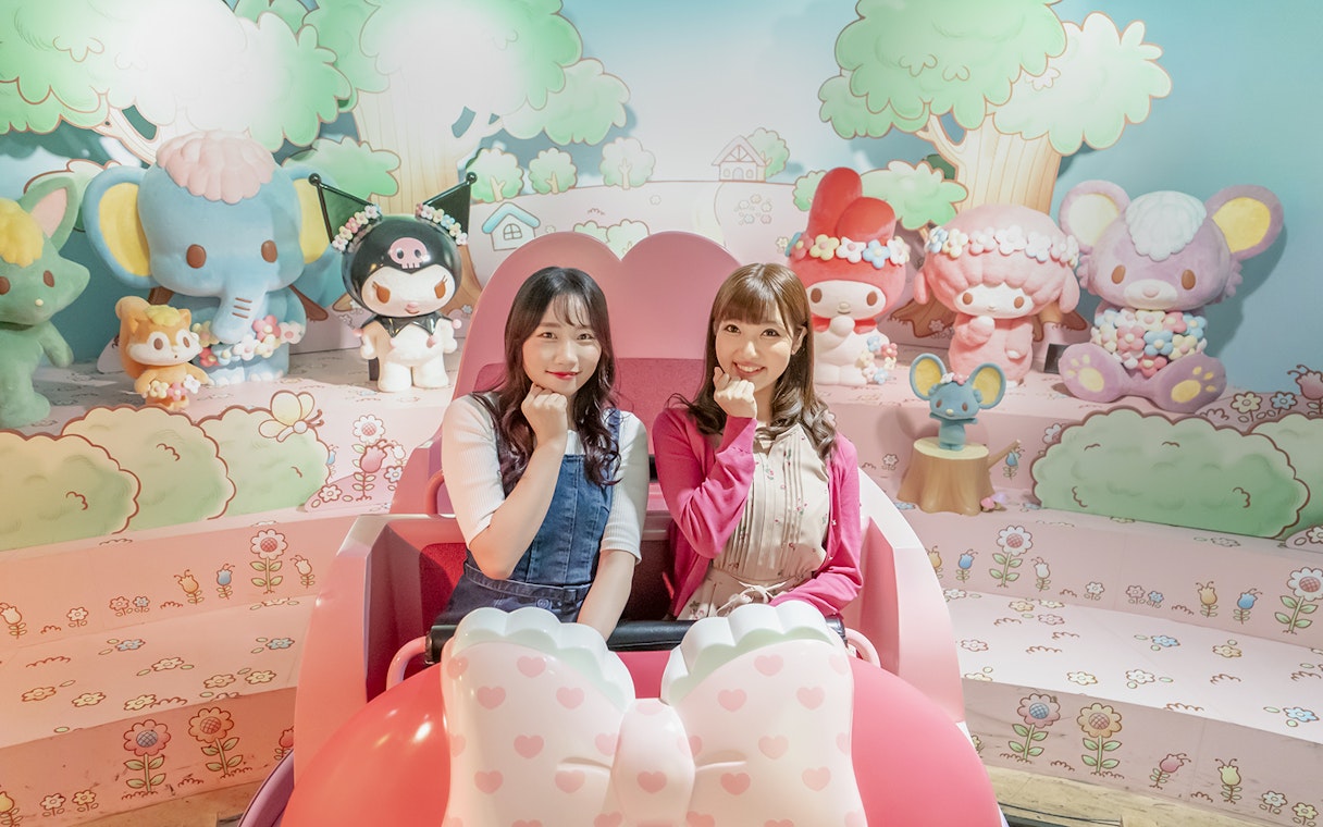 Visitors enjoying a ride at Sanrio Puroland with character figures in the background.