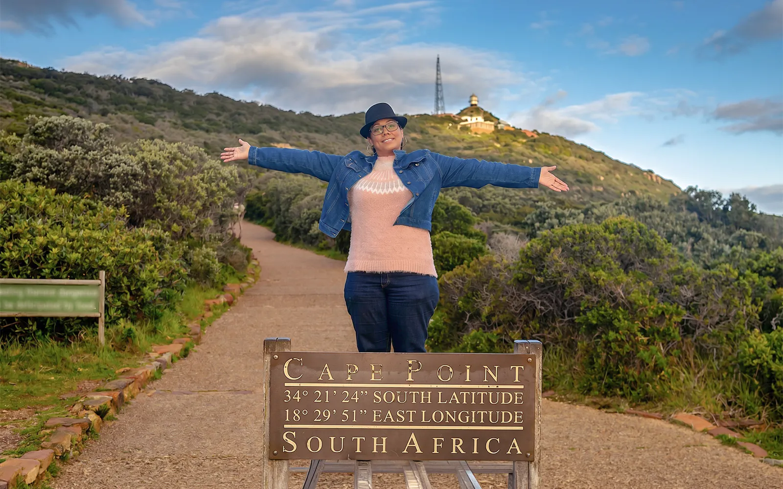 Woman standing with arms outstretched at Cape Point sign, Cape Town, South Africa.