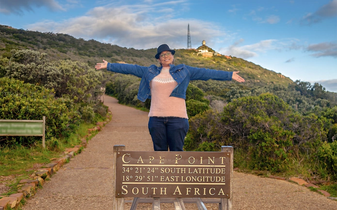 Woman standing with arms outstretched at Cape Point sign, Cape Town, South Africa.
