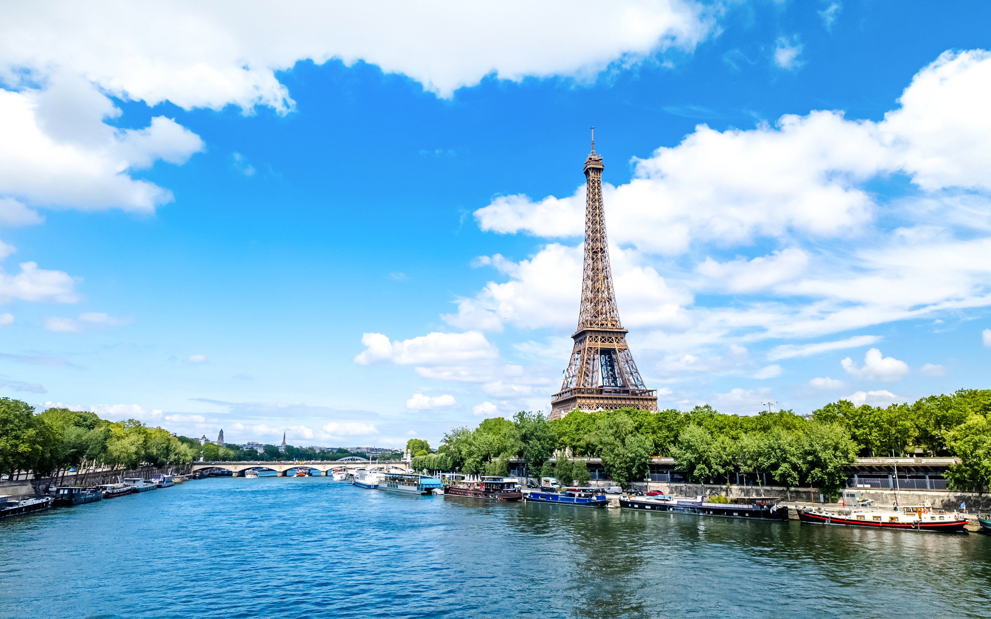 Eiffel Tower beside the Seine River in Paris with boats along the riverbank.