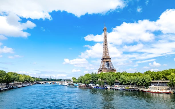 Eiffel Tower beside the Seine River in Paris with boats along the riverbank.