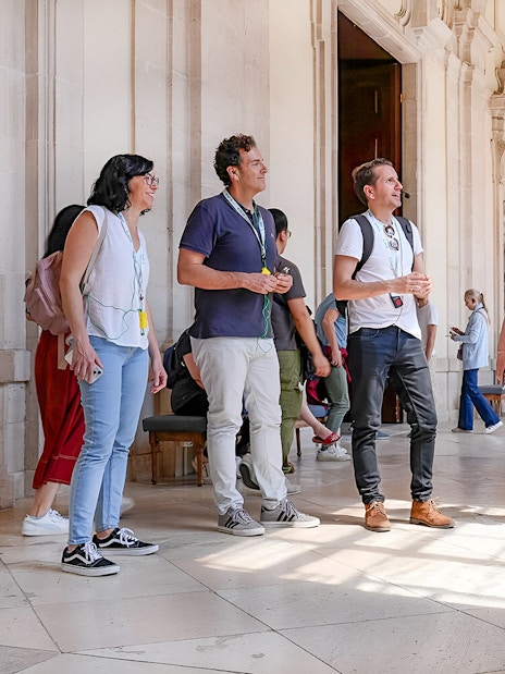 Group on a guided tour at the Prado Museum, Madrid, listening to a guide in a sunlit hallway.