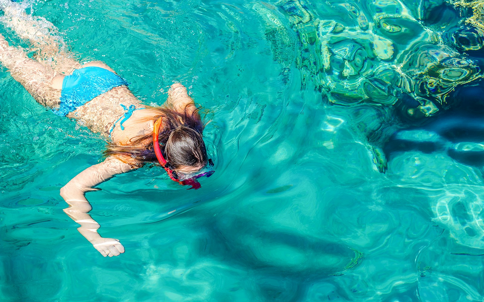 Teenage girl snorkeling in clear blue water.