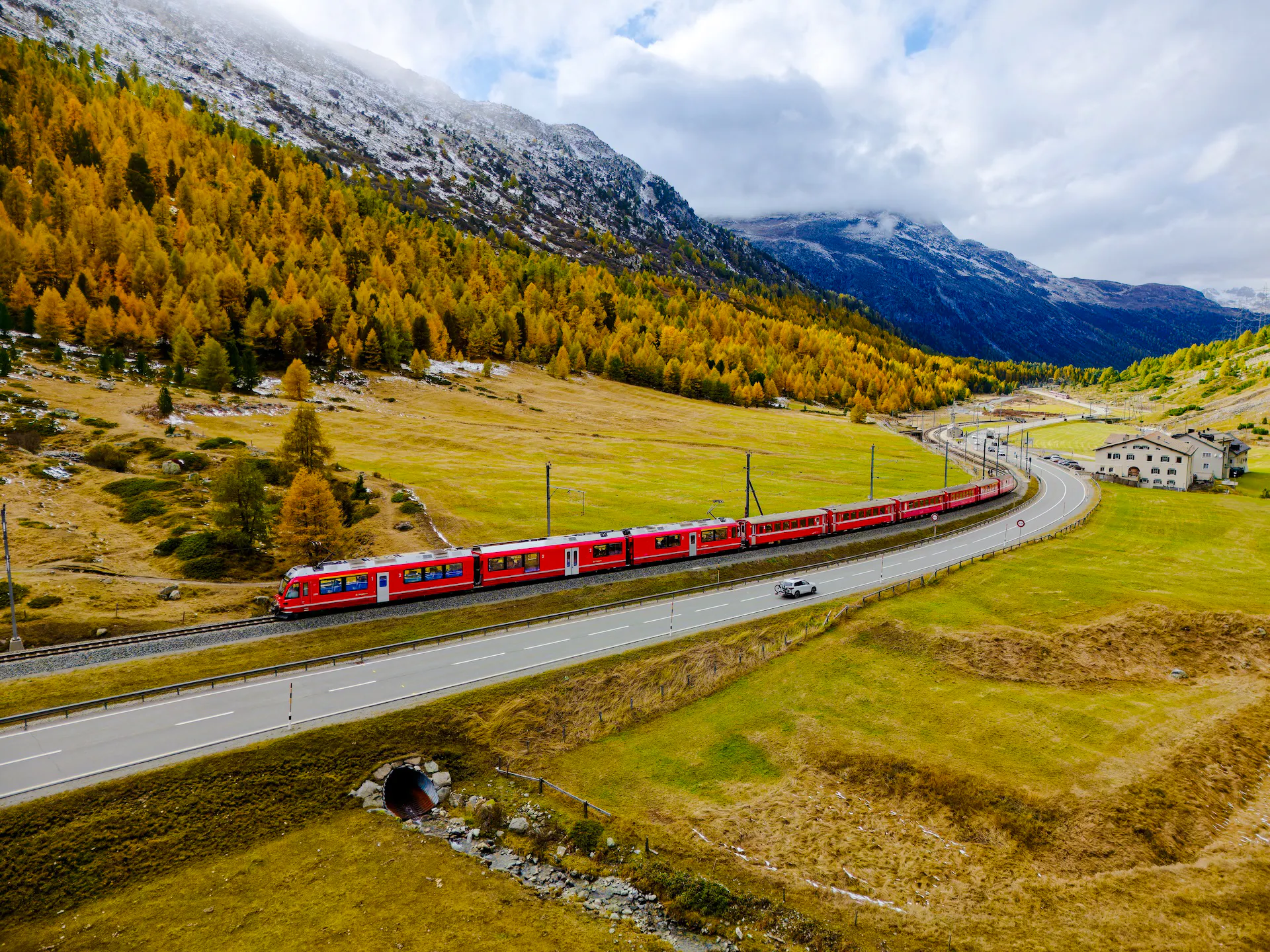Red Bernina train traveling through Swiss Alps landscape near St. Moritz, surrounded by autumn trees.