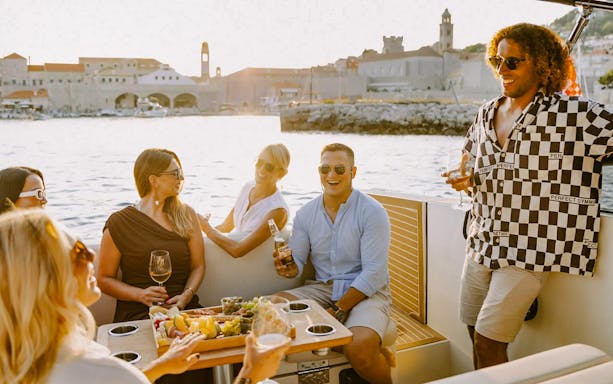 Guests enjoying drinks on a private sunset cruise in Dubrovnik with cityscape in background.