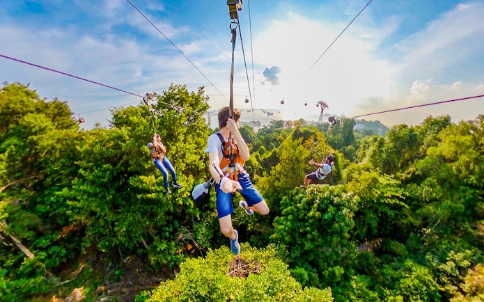 Visitors ziplining over lush greenery at Mega Adventure Park, Singapore.