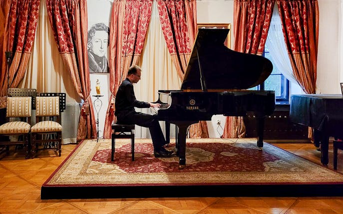 Pianist performing at a Chopin concert in an elegant room with red curtains.