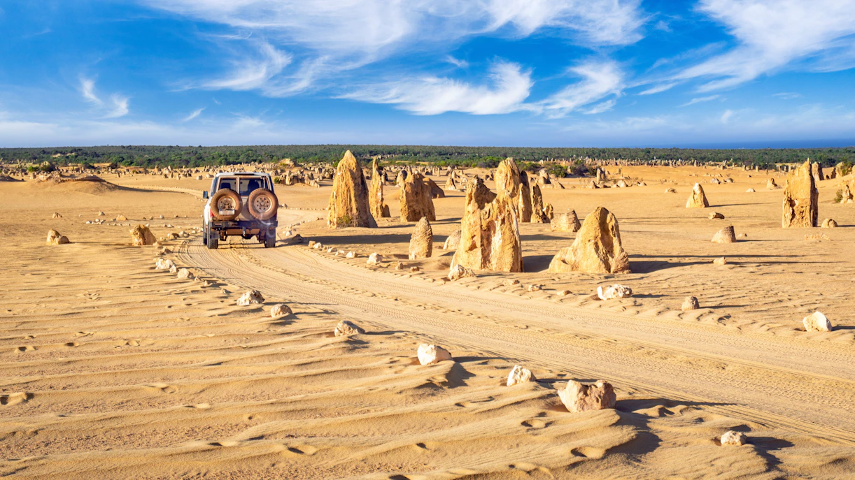 4WD vehicle driving through rocky pinnacles in Nambung National Park, Australia.