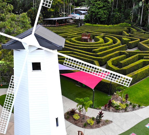 Windmill and hedge maze at Amaze World, surrounded by lush greenery and colorful pathways.