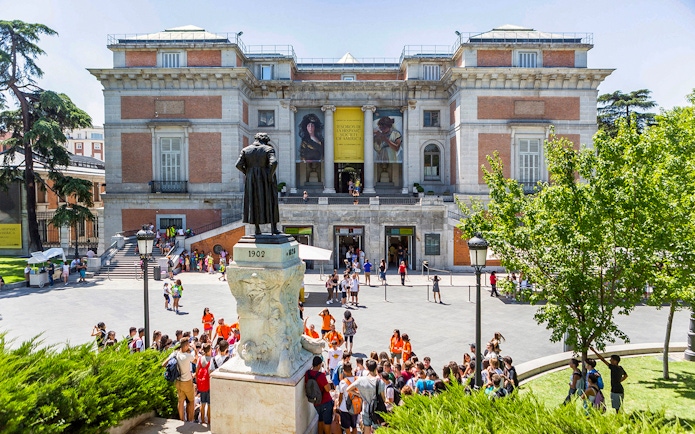 Prado Museum entrance with visitors and statue in Madrid, Spain.