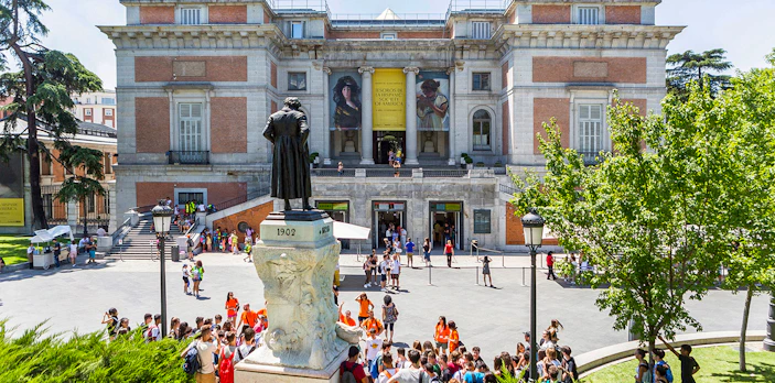 Prado Museum entrance with visitors and statue in Madrid, Spain.