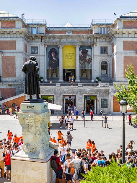 Prado Museum entrance with visitors and statue in Madrid, Spain.