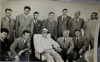 Group of men in suits with a seated individual on the Battleship IOWA President's Tour.